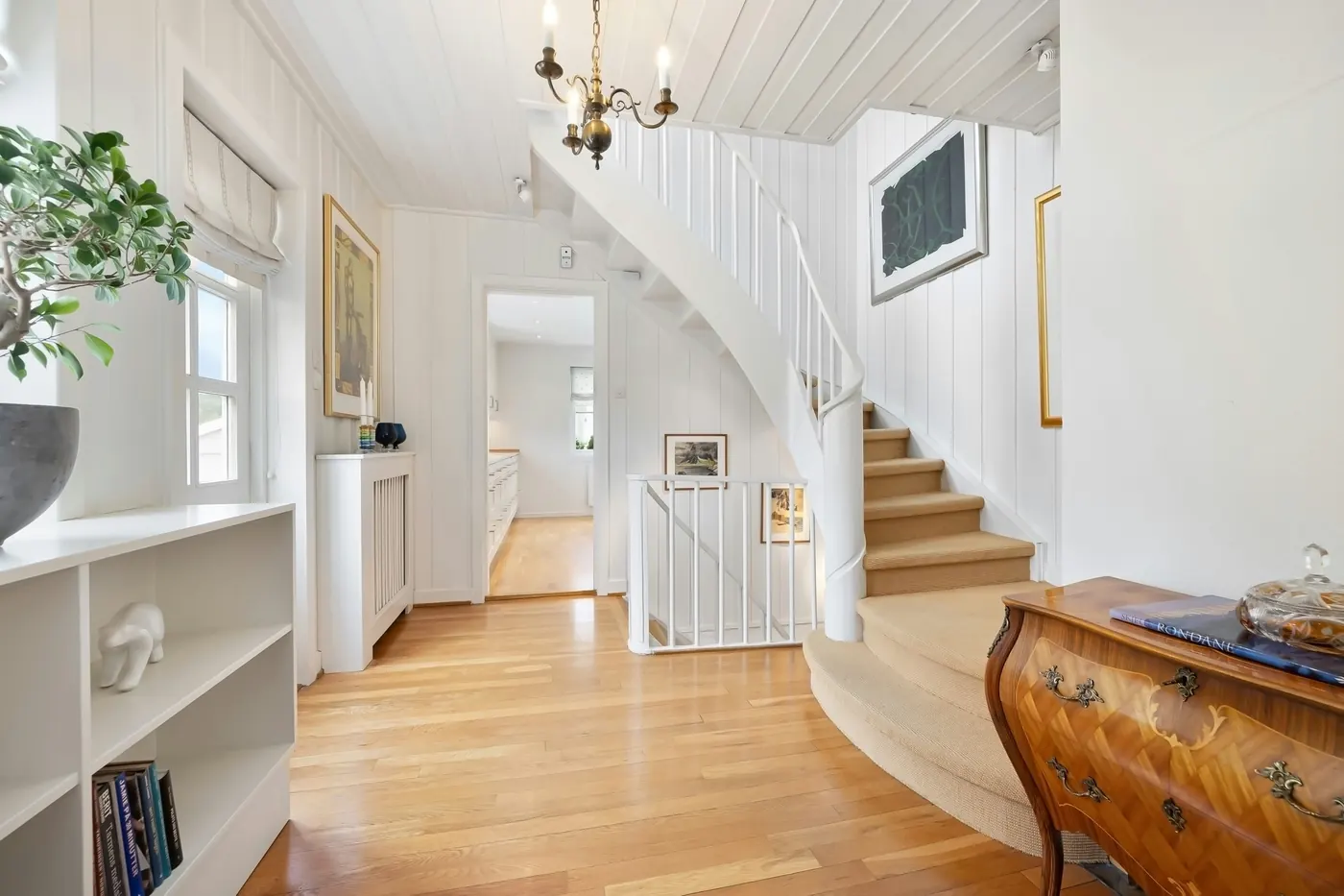 A bright period hallway with a curved staircase and painted panelling